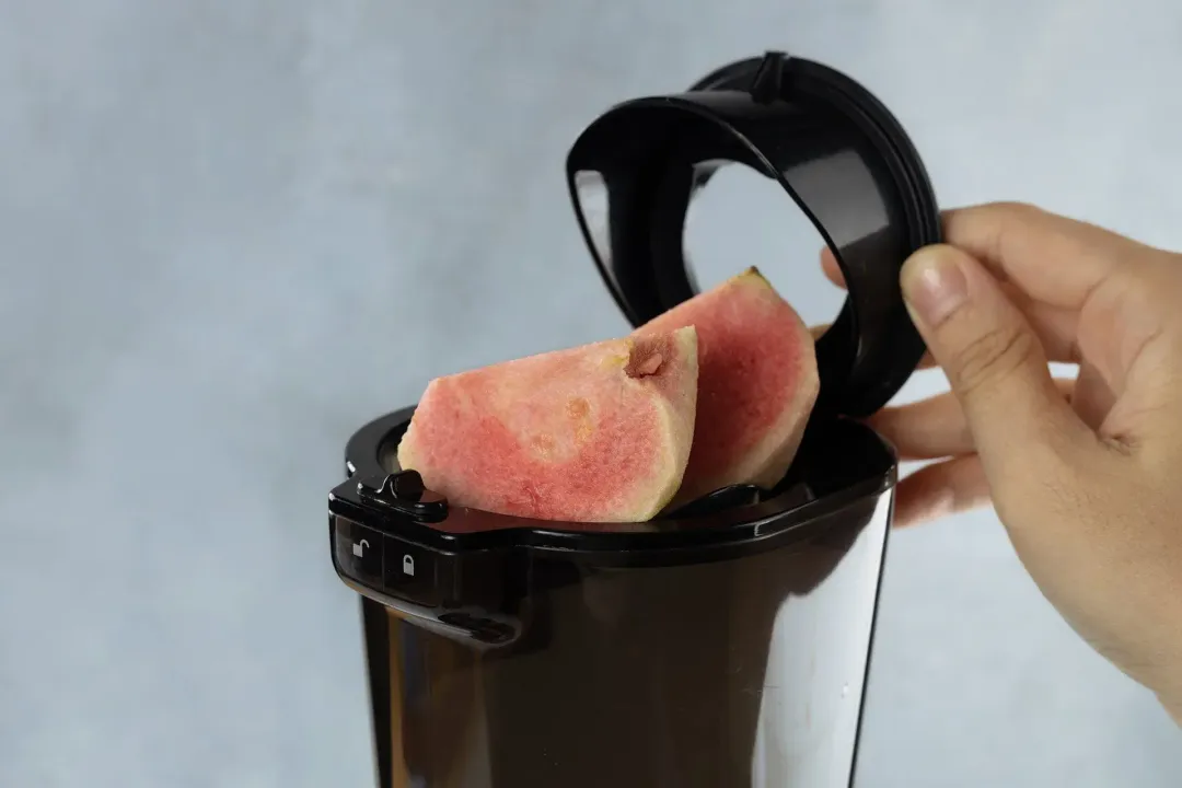 Large pieces of pink guava being put into a juicer