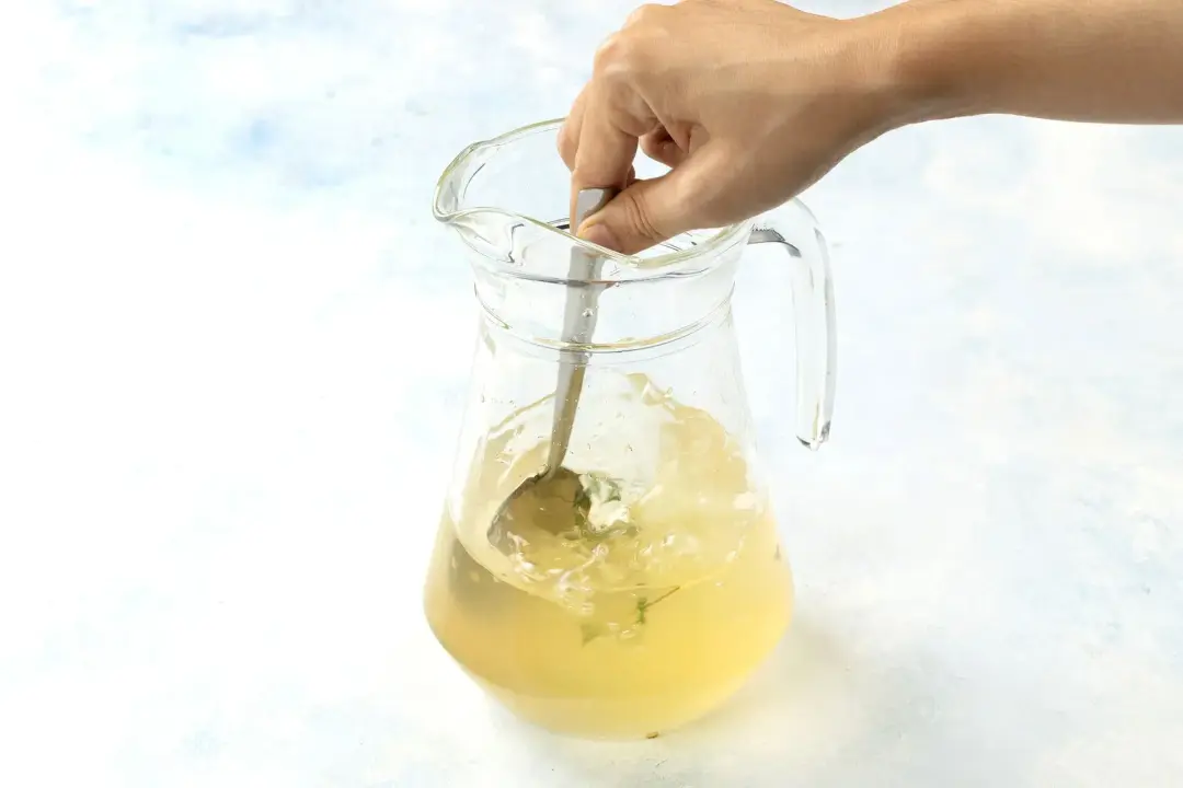 A pitcher of lemonade stirred by a silver spoon