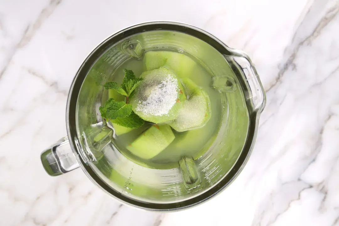 Ingredients in a blender: green kiwis, sugar, and mint leaves