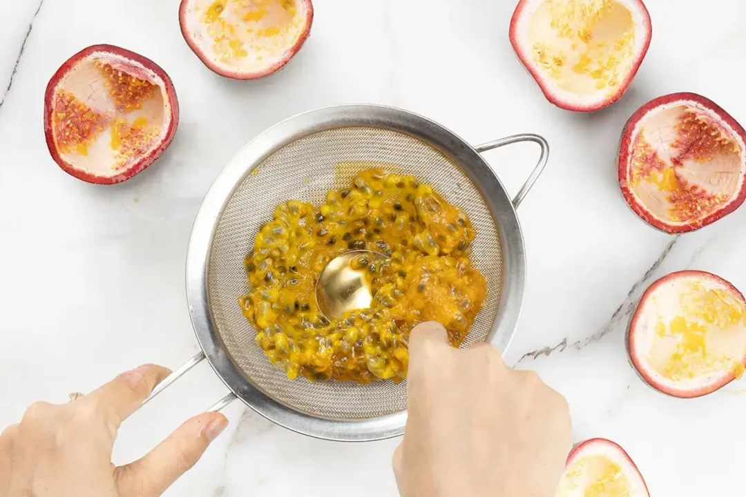 Pressing passion fruit pulps and seeds into a sieve, surrounded by hollow shells of passion fruit