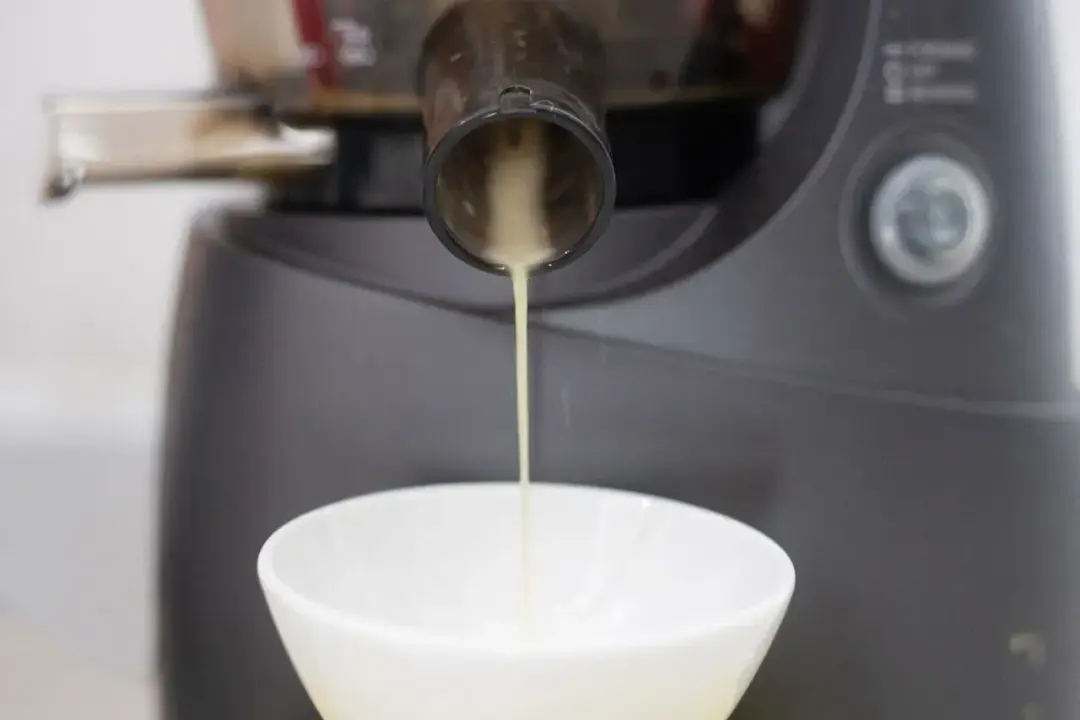 A yellow juice running from one end of a juicer into a white bowl