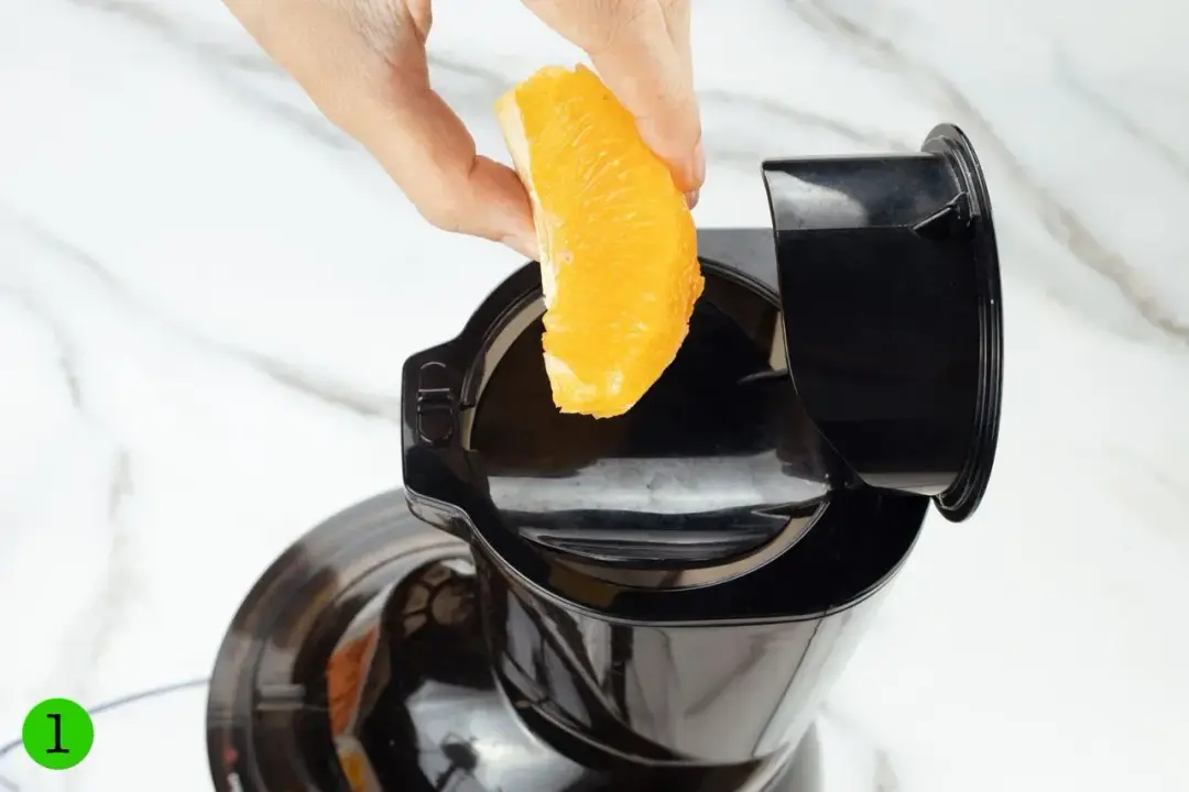 Putting an orange segment into the feeder of a juicer
