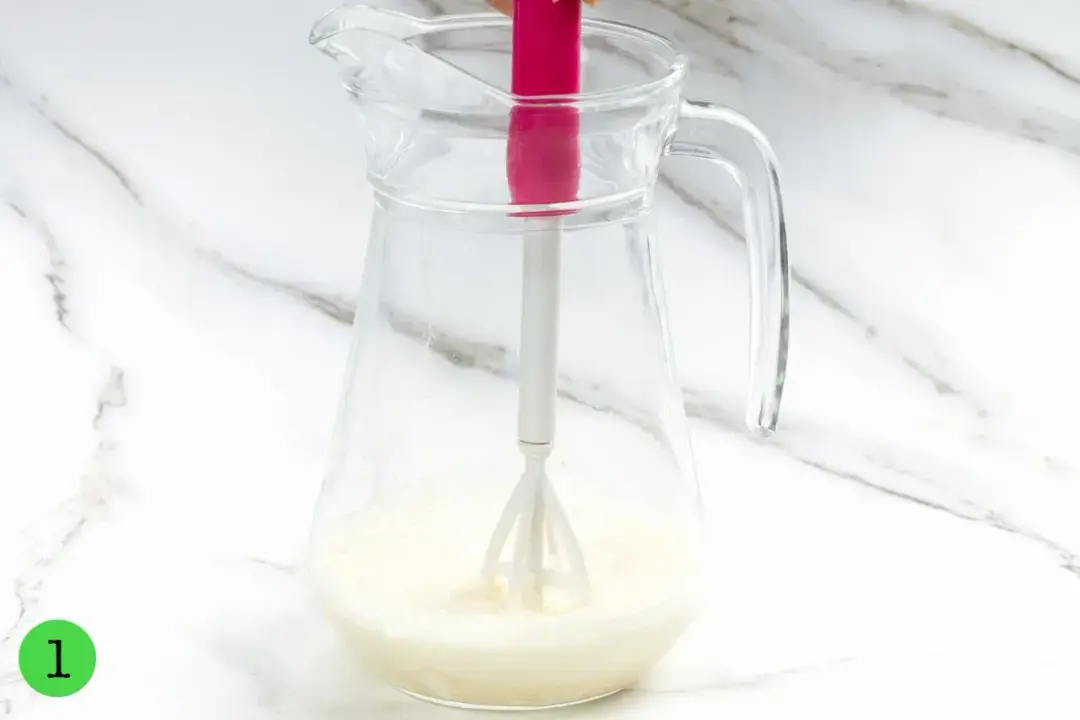 A clear pitcher of milk at the bottom, with a mixer dunked inside
