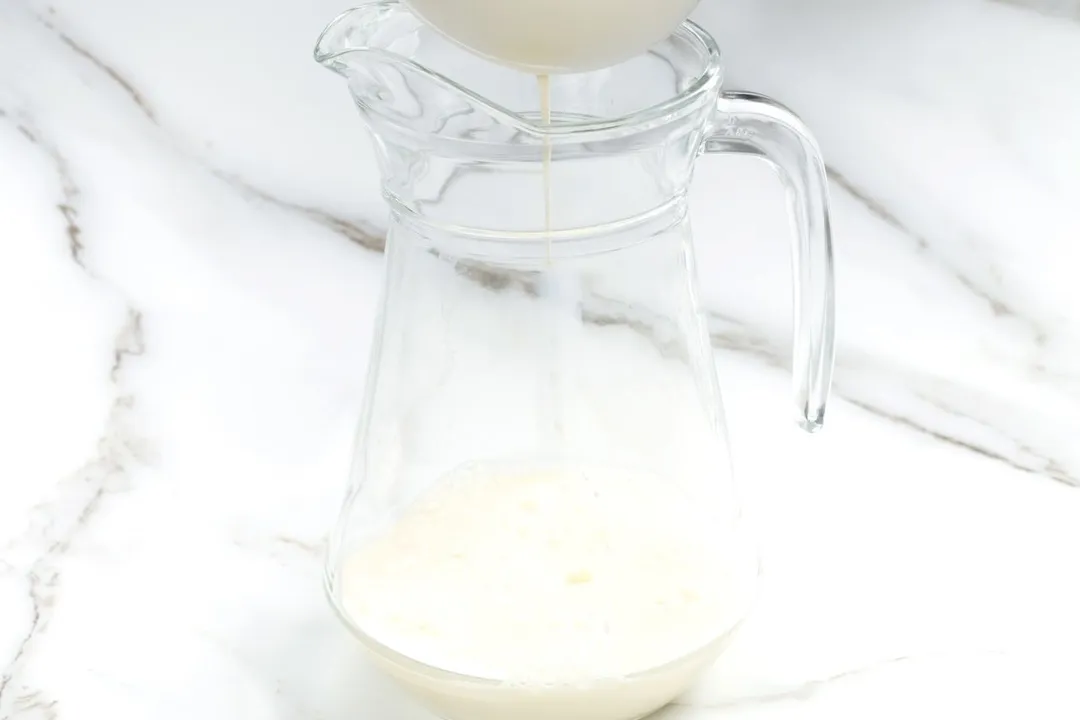 pouring milk from a bowl into a glass pitcher