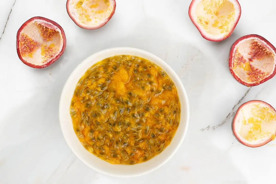 a bowl of passion fruit seed surrounded by half passion fruit