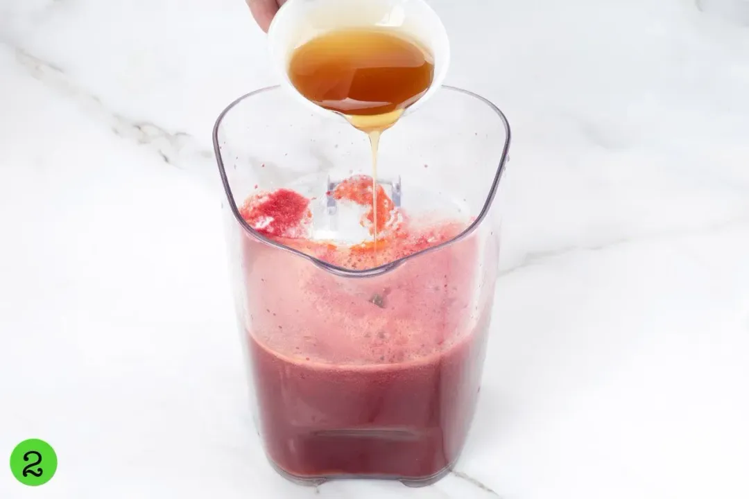 Honey poured into a clear pitcher of red beetroot juice