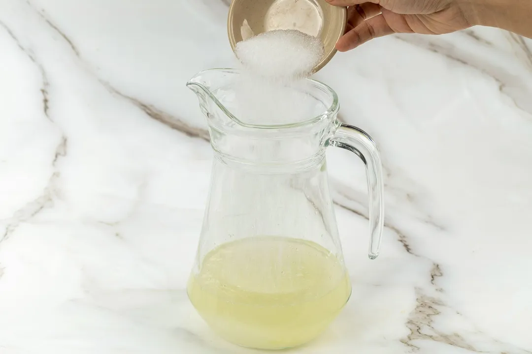 pour sugar from a small bowl into a glass pitcher