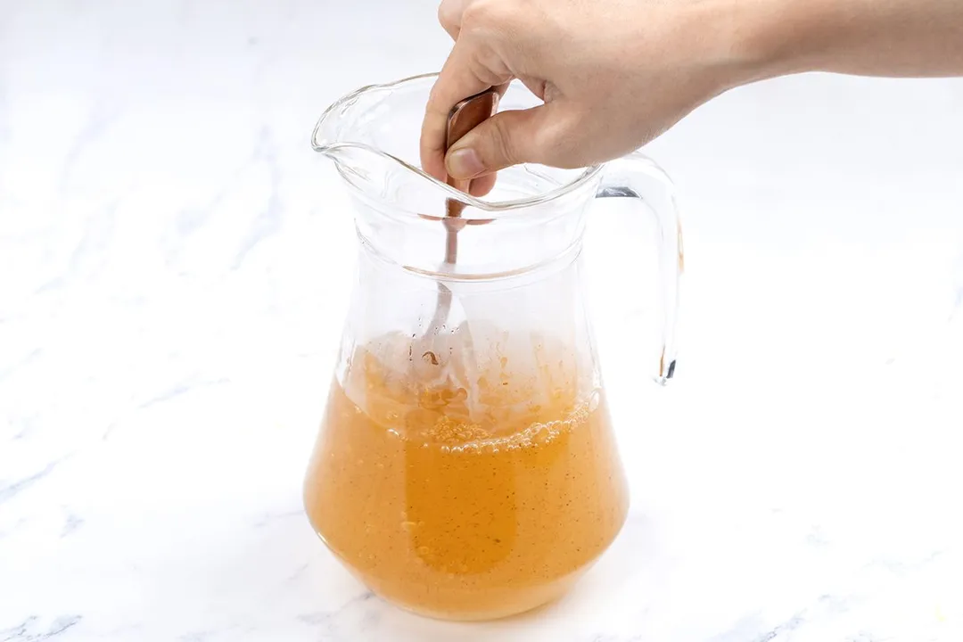 a hand holing a spoon stir liquid in a jar