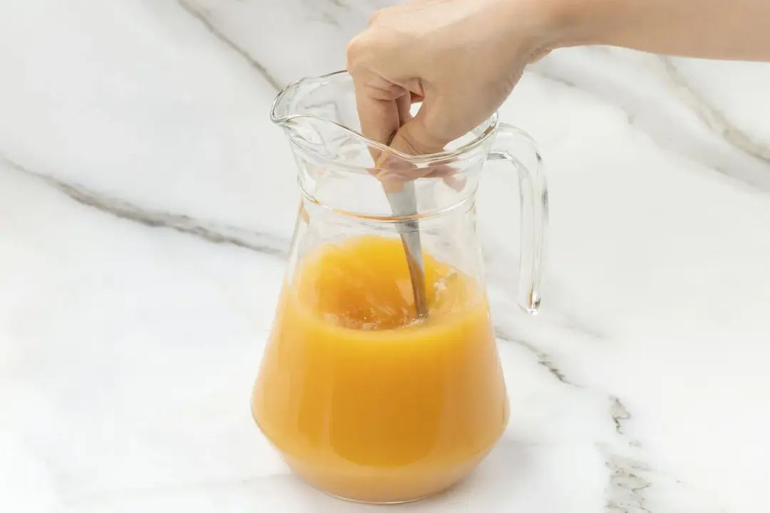 Stirring a clear pitcher of grapefruit juice