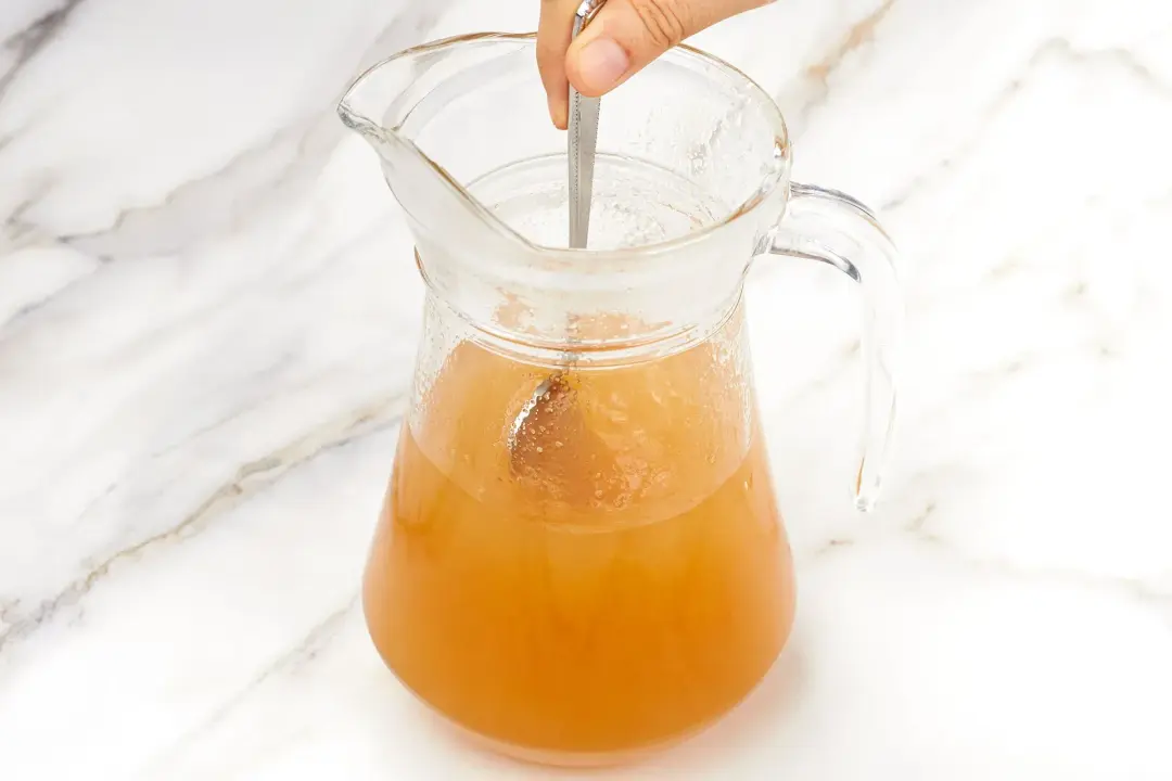A glass pitcher of hot toddy stirred with a silver spoon