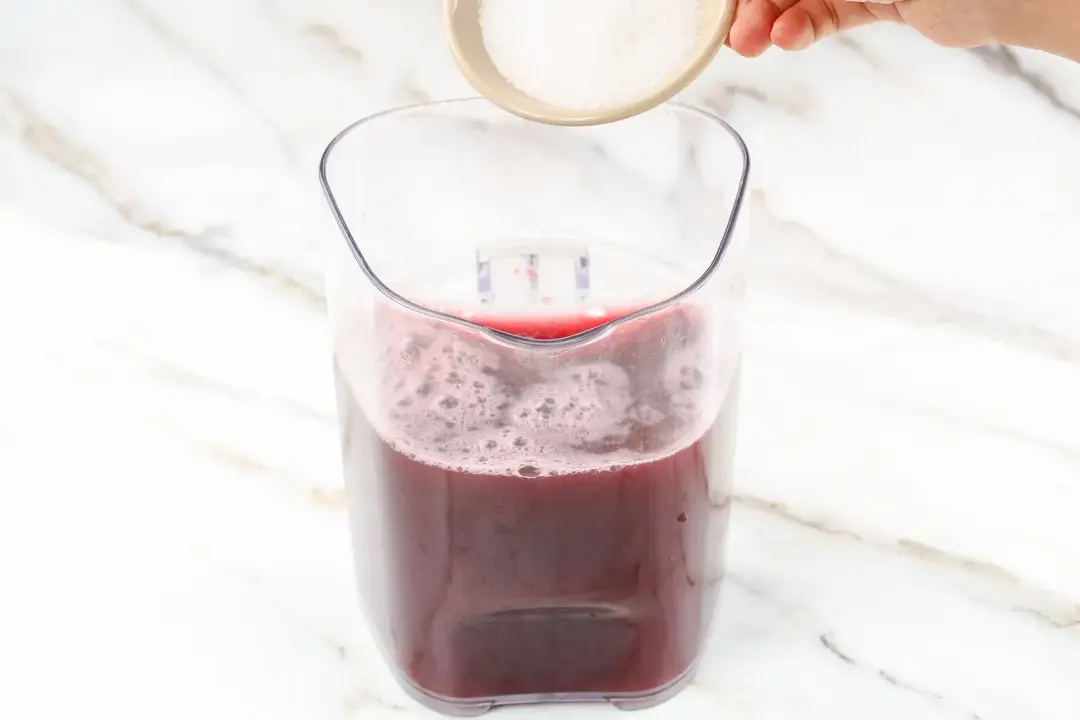 Putting sugar into a pitcher half-filled with pink blackberry drink