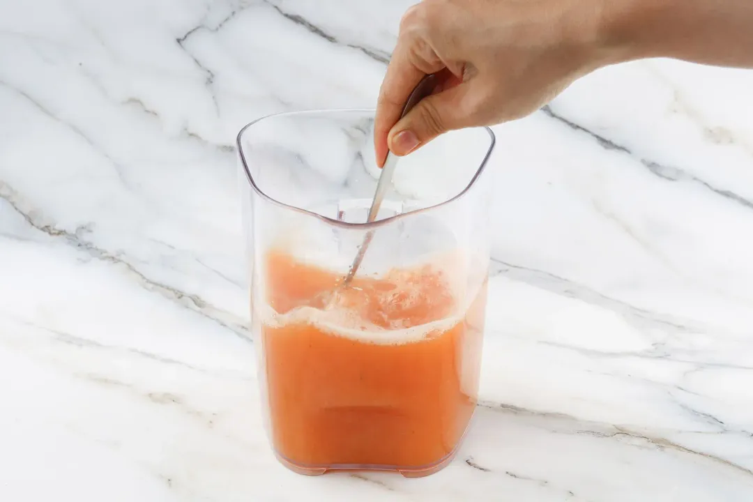 Cantaloupe juice stirred inside a glass pitcher with a silver spon