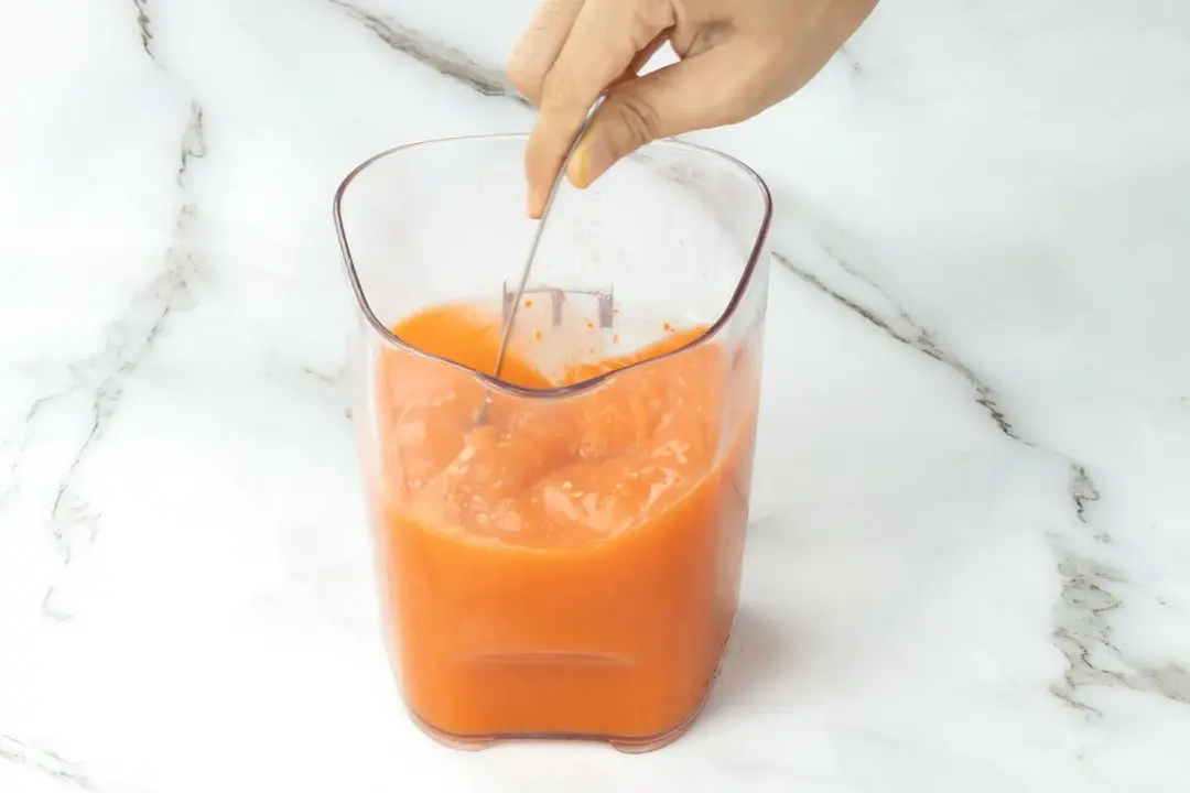 Stirring an orange juice in a clear glass pitcher