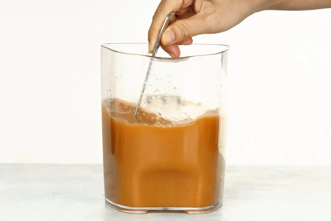 A hand stirring a pitcher of brown-orange liquid