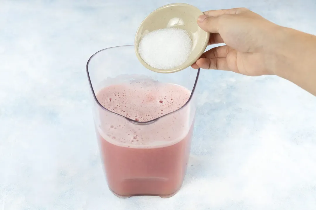 Sugar being put into a large juice container holding pink guava juice