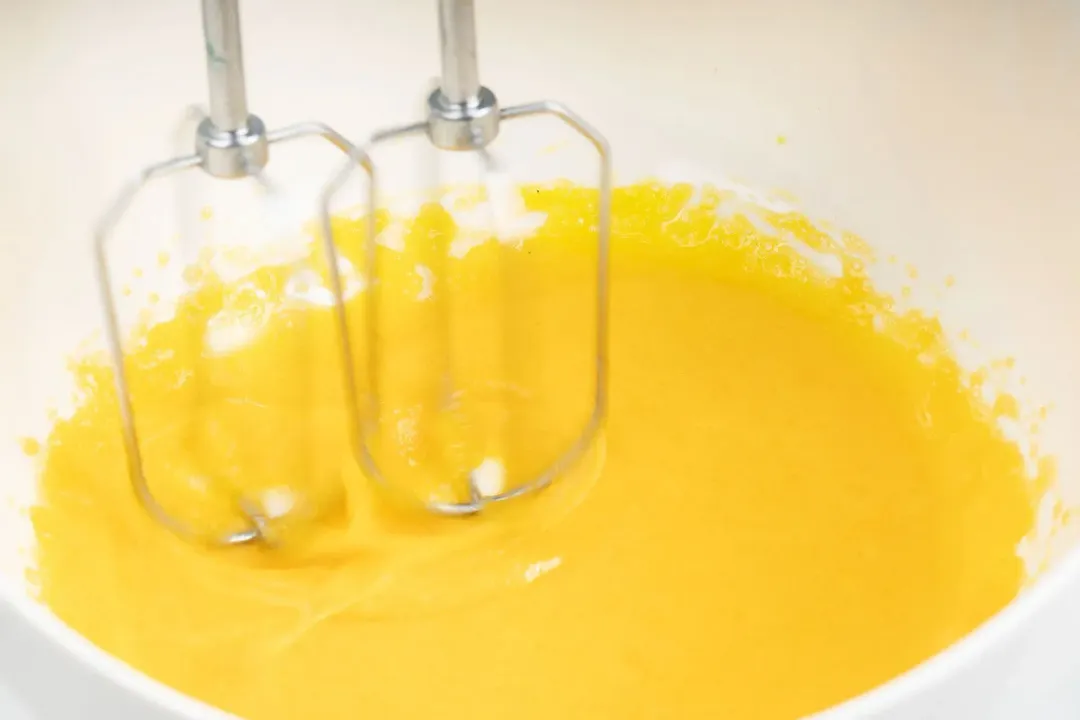 Milk pouring into some beaten egg yolks