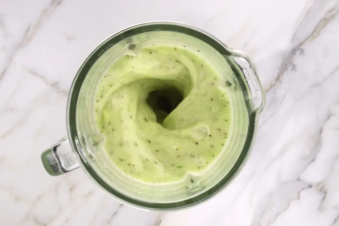 A blender blending a green kiwi mixture, with vivid seeds