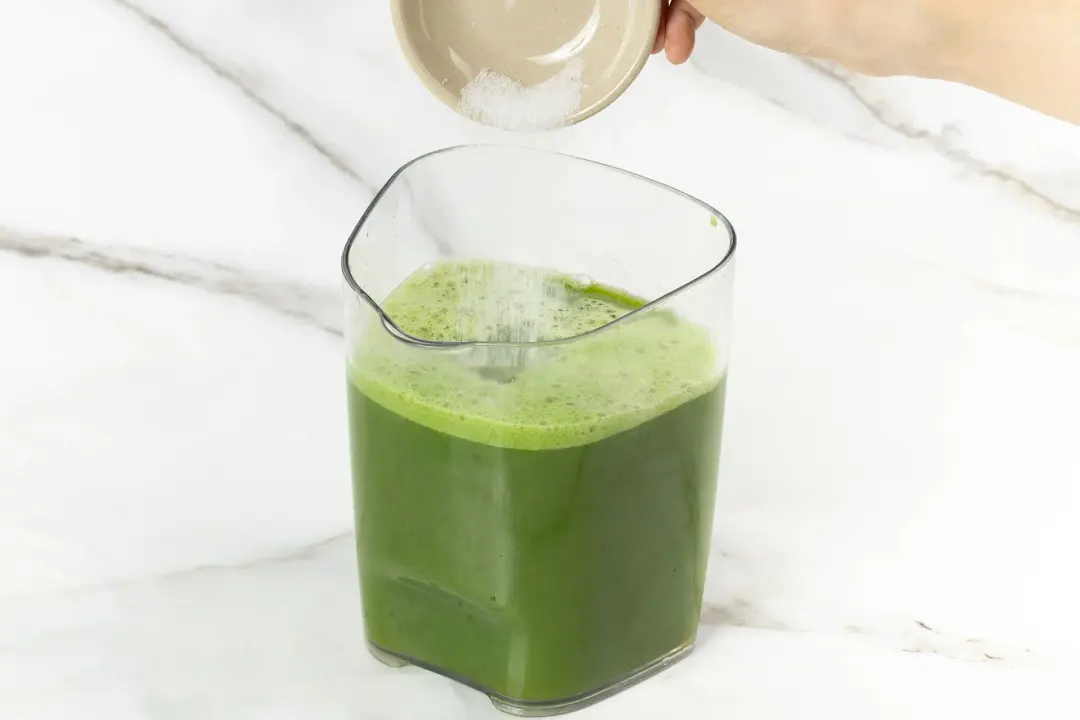 Granulated sugar added to a large pitcher of green juice