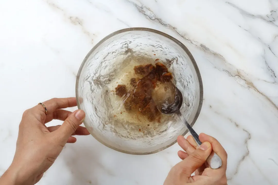 A hand mashing some tamarinds soaked in a bowl of clear water