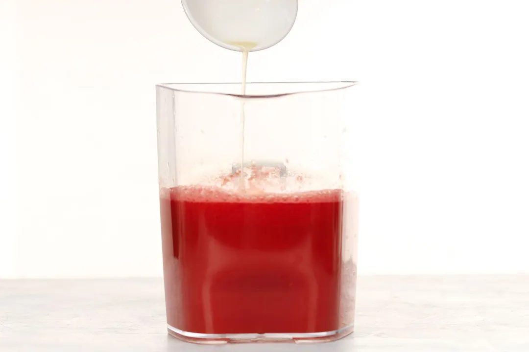 Lime juice being drizzled into a large glass jug filled up to two-thirds with watermelon carrot juice.