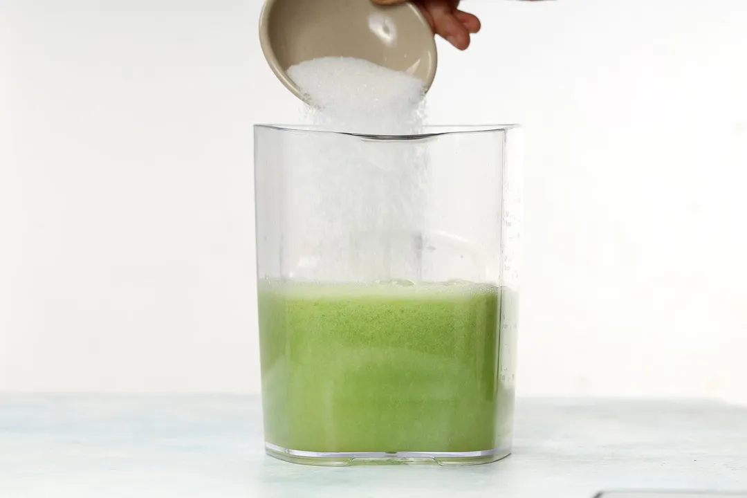 Sugar being poured into a large jug half-filled with winter melon juice.