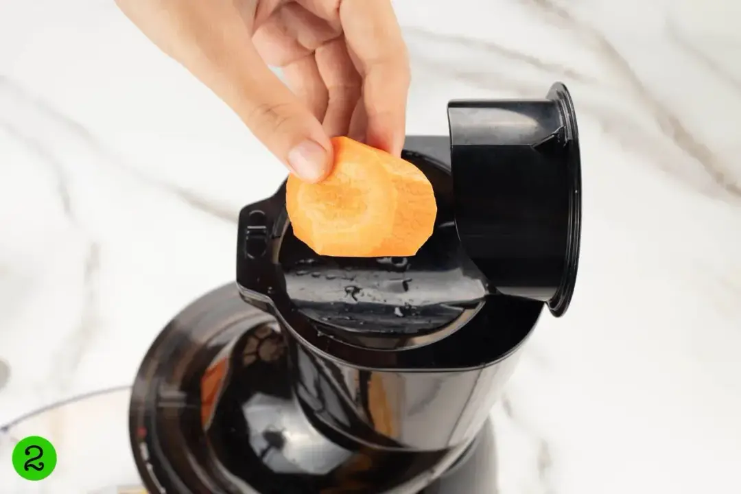 Putting a carrot slice into the feeder of a juicer