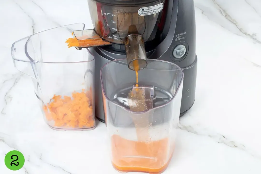 A juicer emitting juice into a glass pitcher on one end and fruit pulps into a clear container on the other end