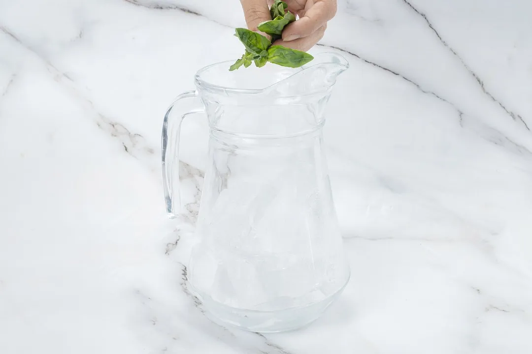 hand holding basil leaves on top of a jar