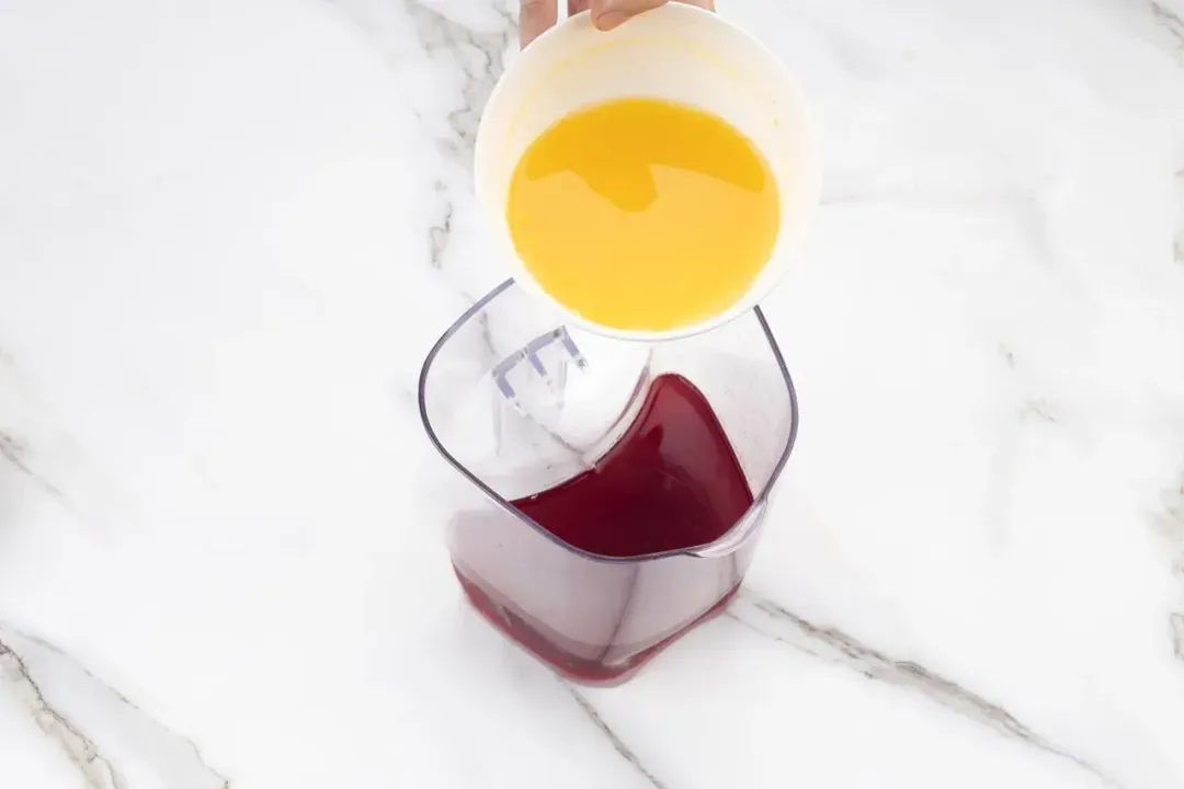 A small bowl of orange juice hovered over a container of pomegranate juice