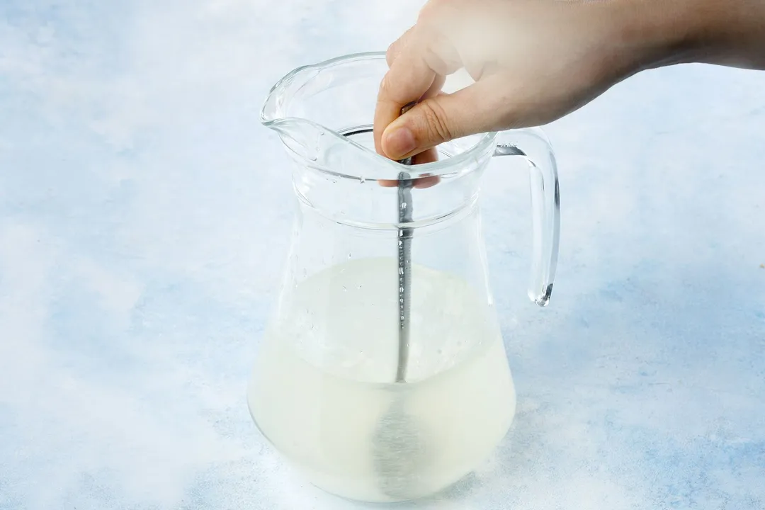 a hand holding a spoon in a glass pitcher of fresh lime juice