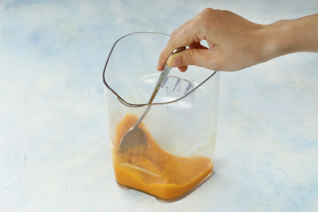 hand holds a spoon to whisk orange liquid in a pitcher