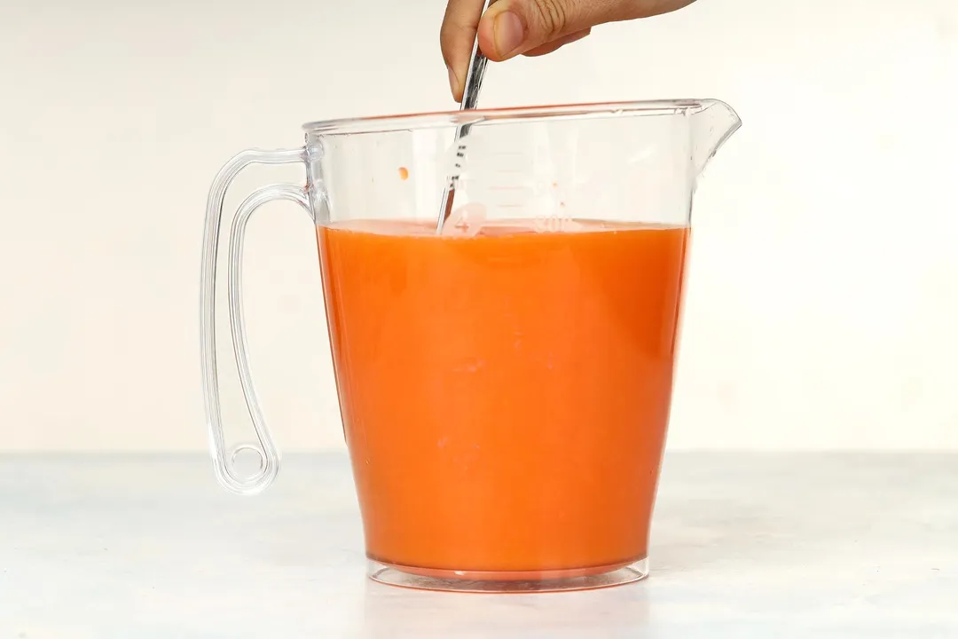 whisk orange liquid in a pitcher by a spoon
