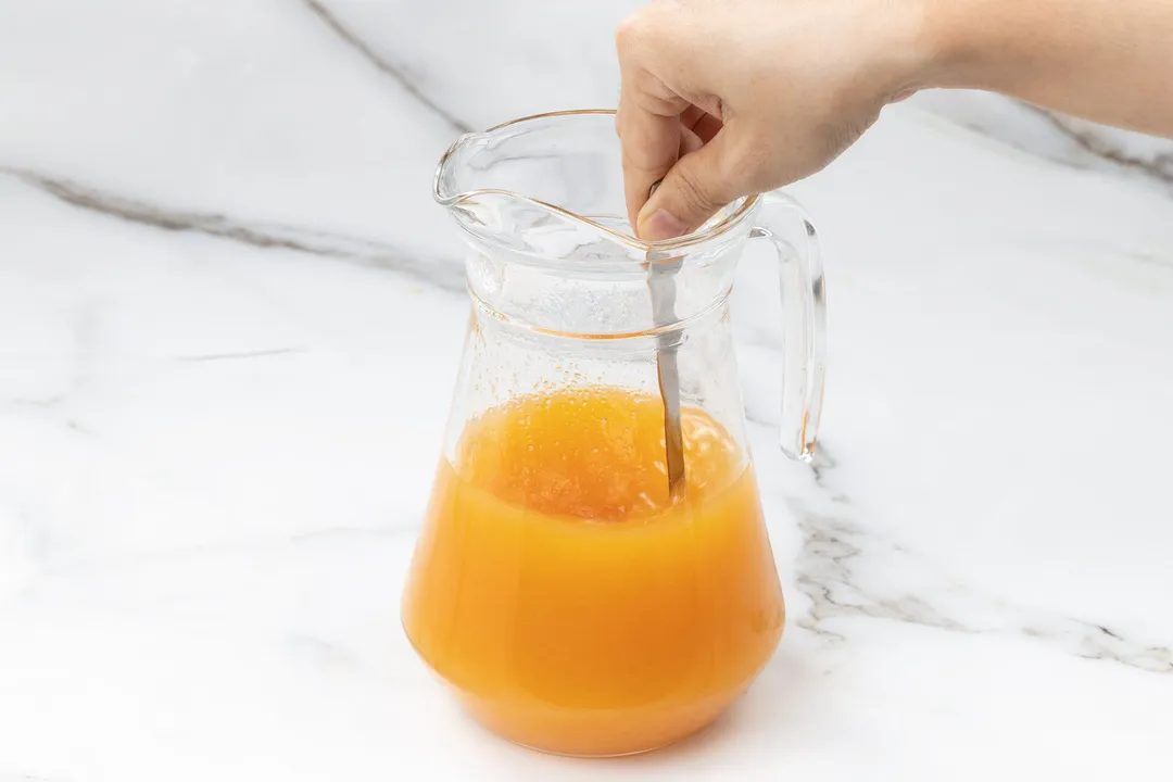 a hand holding a spoon in a glass pitcher of orange liquid