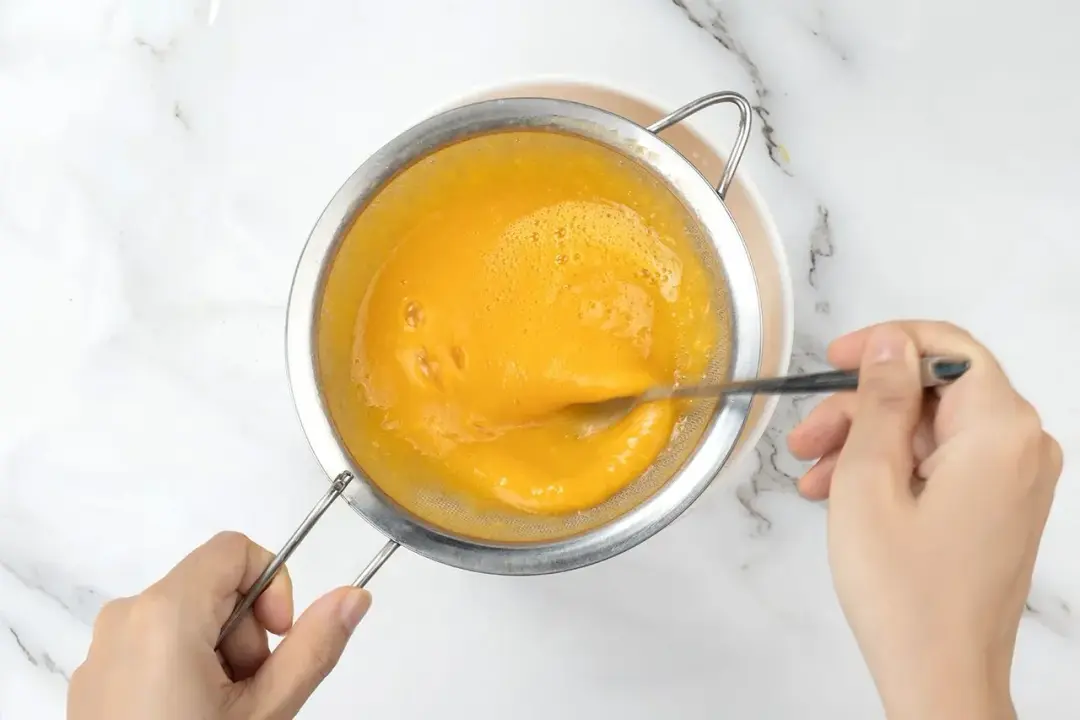 Running a mango smoothie mixture through a sieve