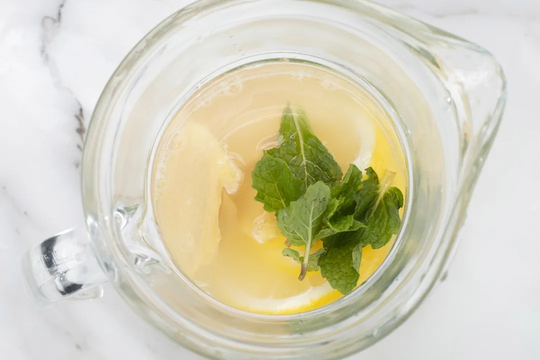 top view of glass ginger slices, lime slices, lemon slices and mint leaves in a glass pitcher