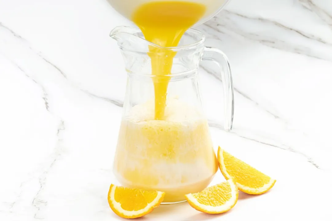 pouring orange juice from a bowl into glass pitcher