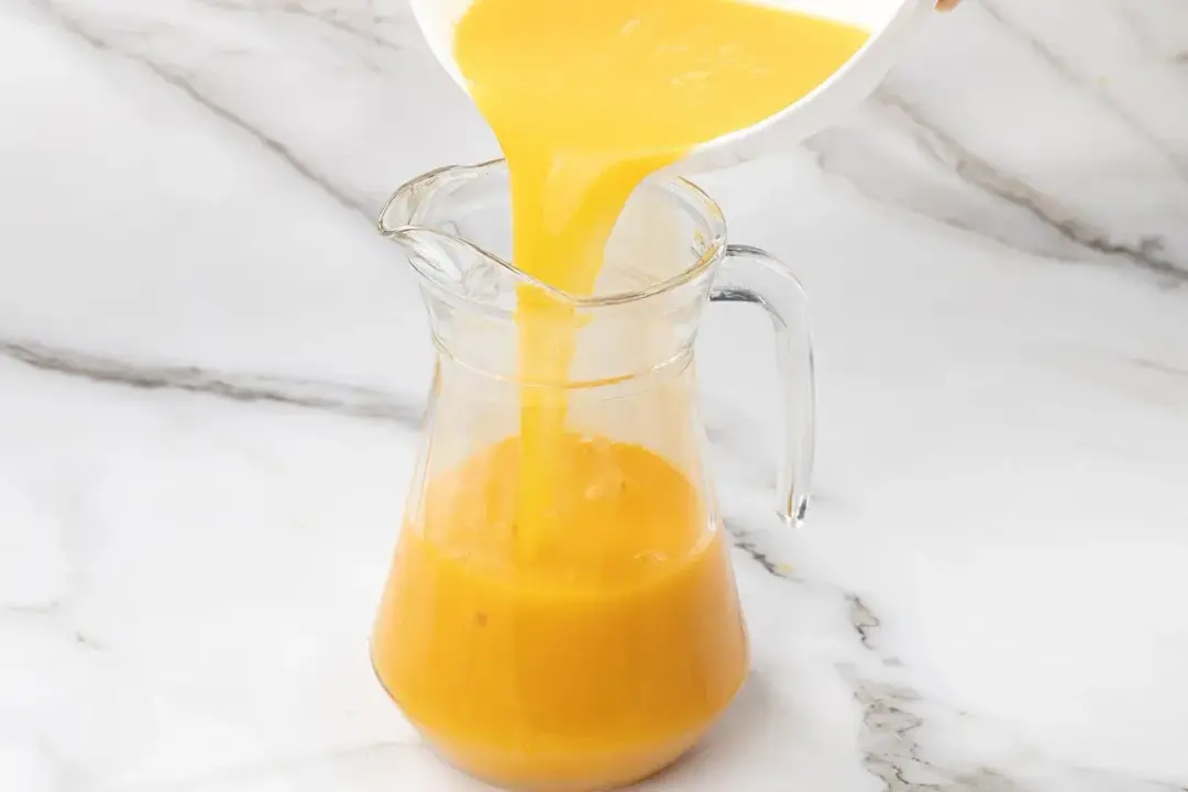 Pouring some orange juice into a pitcher filled with mango juice