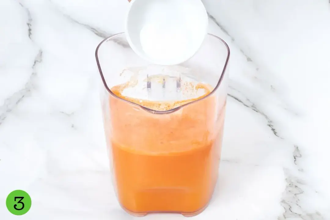 Pouring sugar into a clear pitcher of orange carrot pineapple juice