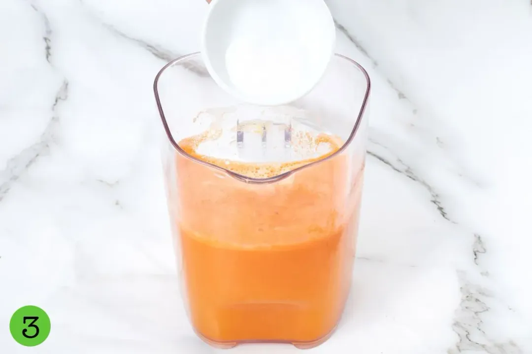 Pouring sugar into a clear pitcher of orange carrot pineapple juice