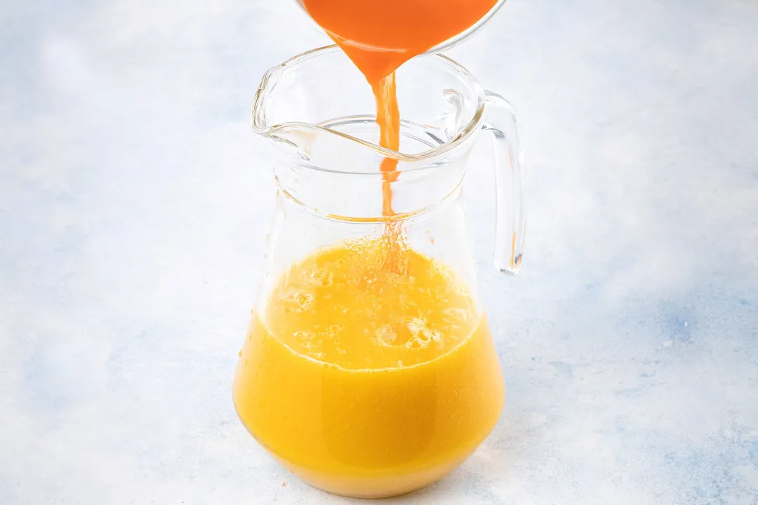 pouring carrot juice into a glass pitcher