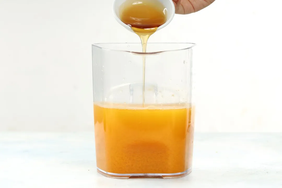 pouring honey from a small bowl to a pitcher of orange liquid