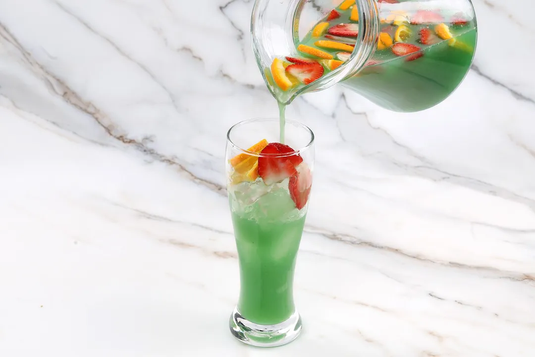 a large pitcher of green jungle juice pouring into a glass