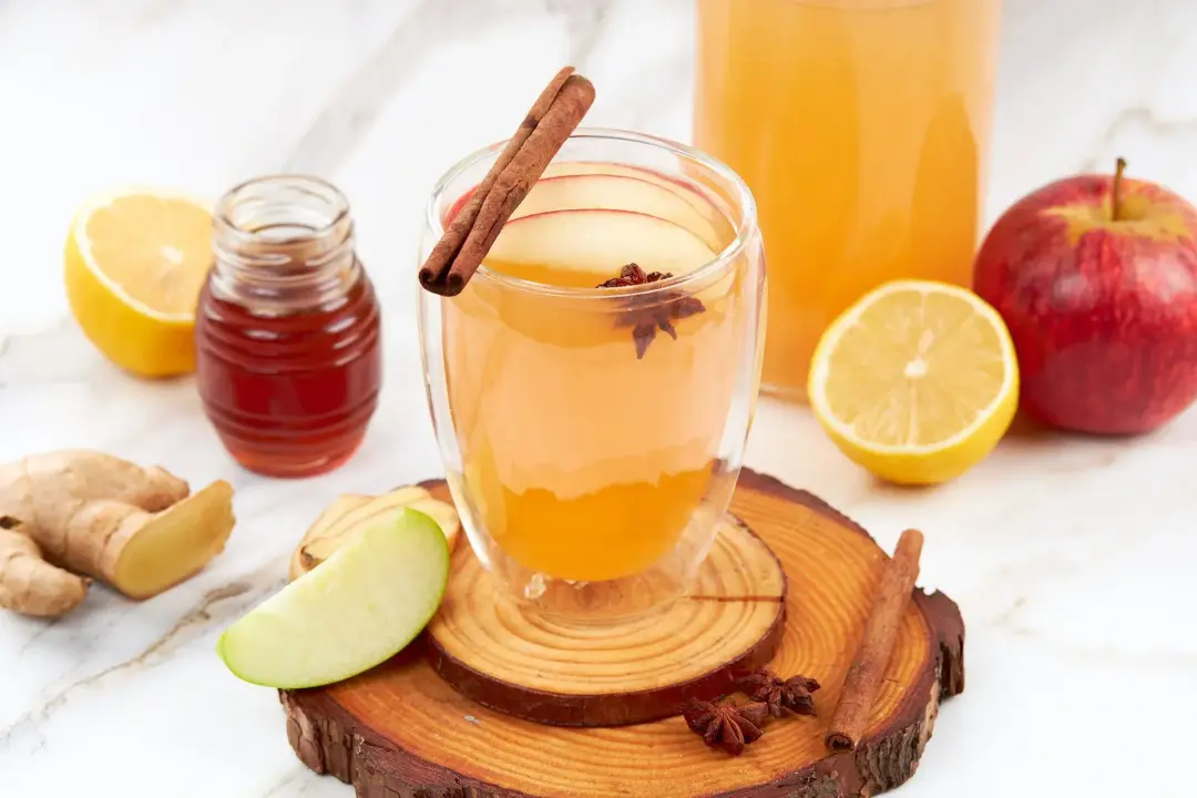 A glass of hot toddy with a star anise, a cinnamon stick on top, and apple, orange around as garnish