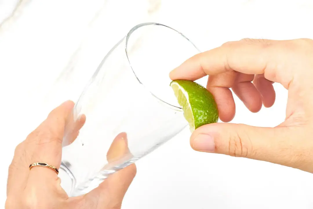 Two hands running a lime wedges along the rim of a tall glass