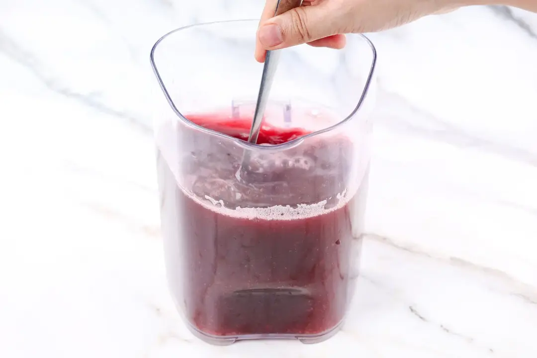Stirring a dark red blackberry drink in a pitcher