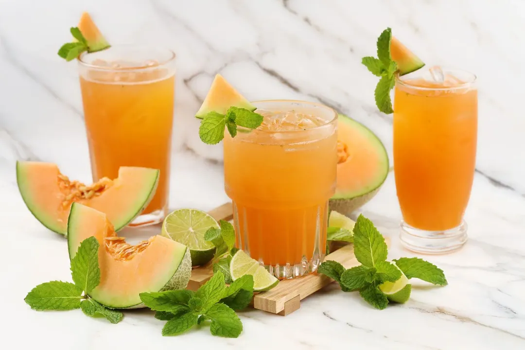 Three iced glasses of cantaloupe drinks, garnished with cantaloupe wedges and lots of mints