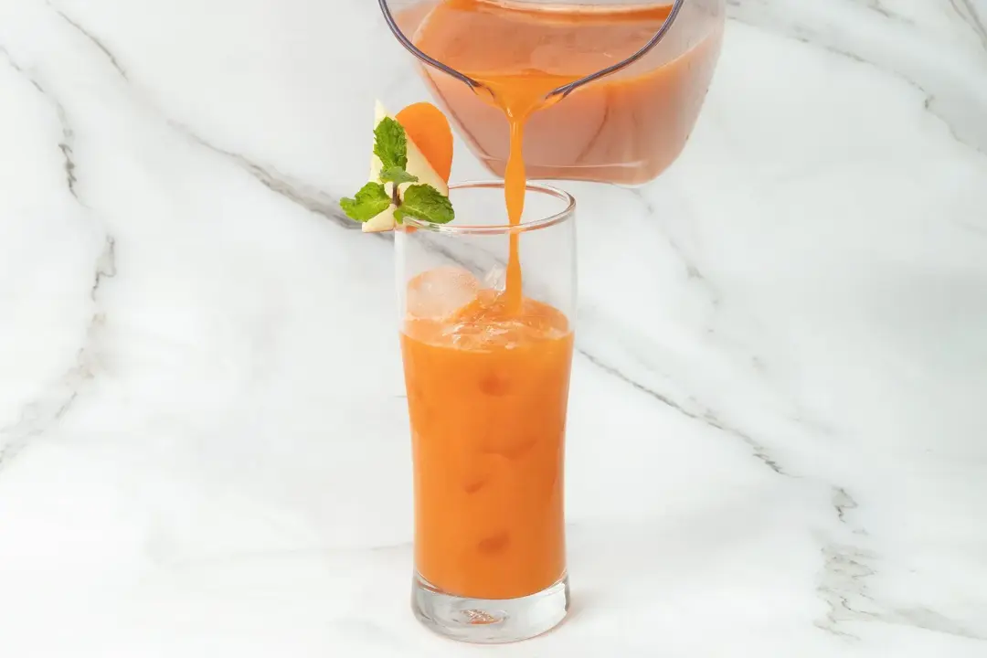 Pouring an orange drink into an iced glass with mints and carrot slices