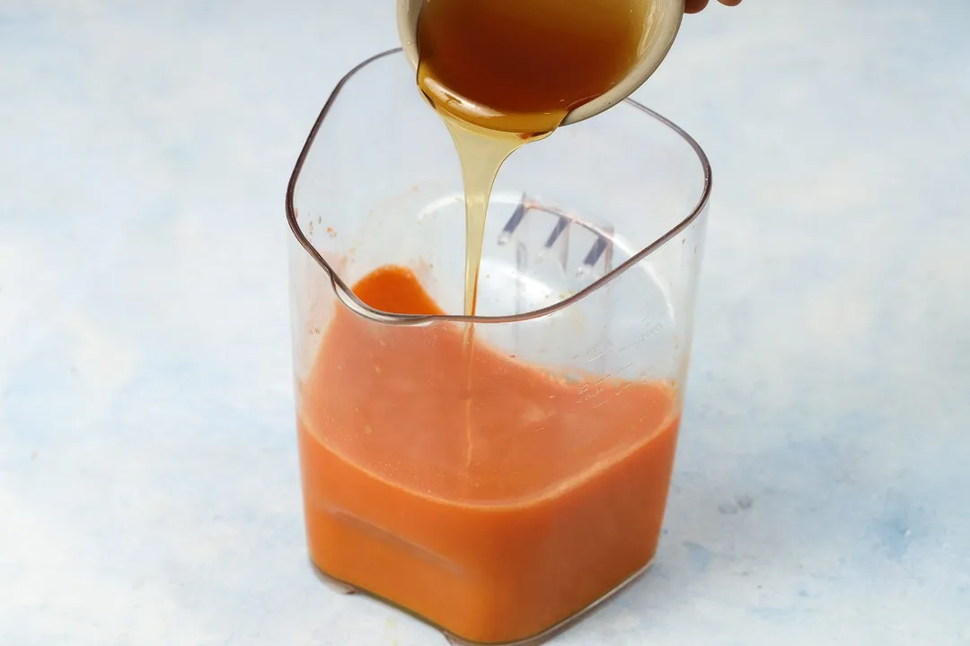A spoon distributing honey into a jug of Carrot Ginger Turmeric Juice.