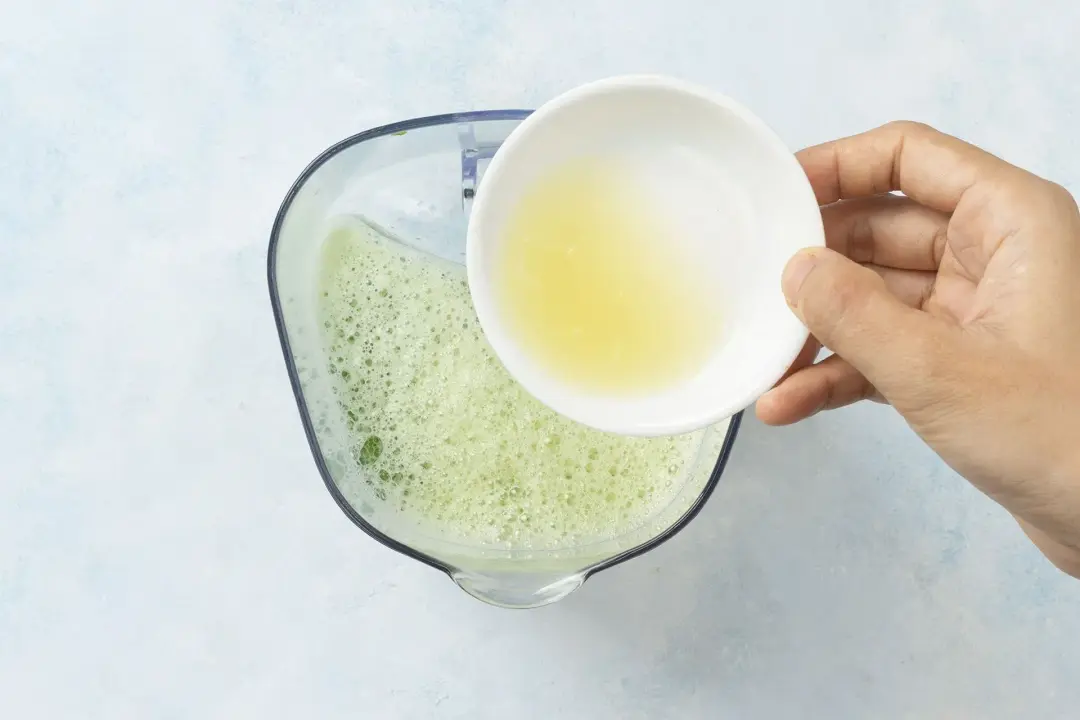 Lemon juice about to be poured into a pitcher of bubbling cucumber juice