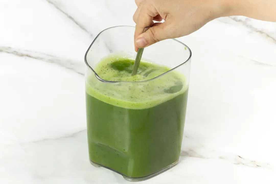 A large pitcher of green juice stirred by a hand